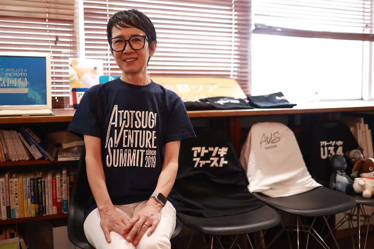 アトツギベンチャーサミットのTシャツを着てオフィスで微笑む一般社団法人ベンチャー型事業承継 代表理事 山野千枝氏